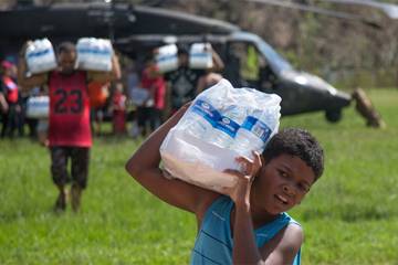 A young boy carries a case of water away from a helicopter in Puerto Rico