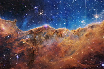 An apparent landscape of mountains and valleys speckled with glittering stars is actually the edge of a nearby, young, star-forming region called NGC 3324 in the Carina Nebula in this image captured by the James Webb Space Telescope